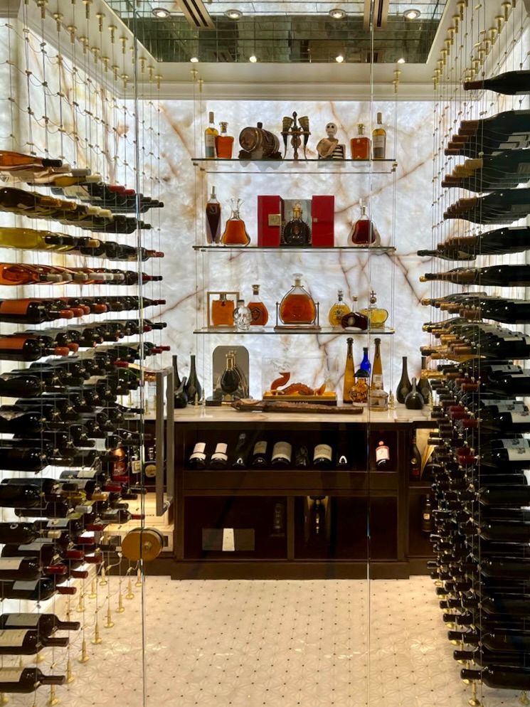 A luxury wine cellar with glass-enclosed racks, glowing marble walls, and a central display of liquor bottles.