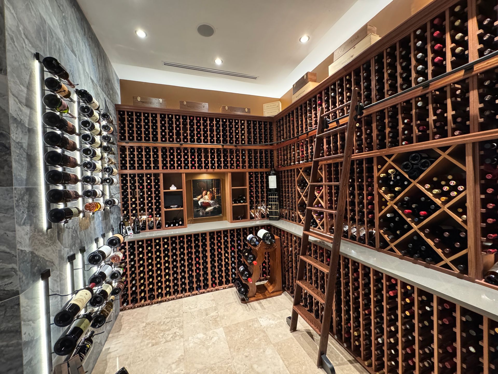 A wine cellar with extensive wooden racks filled with wine bottles, stone wall accents, lighting, and a rolling ladder.
