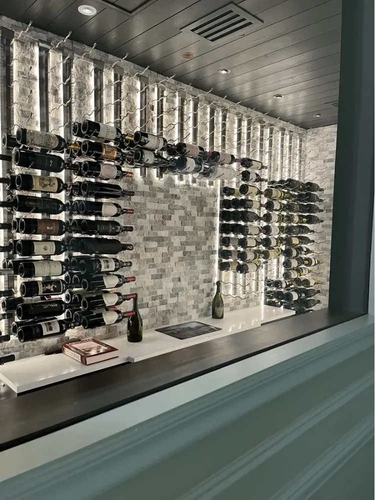 A wine rack display featuring rows of bottles on metal prongs against a white brick wall above a sleek bar counter.