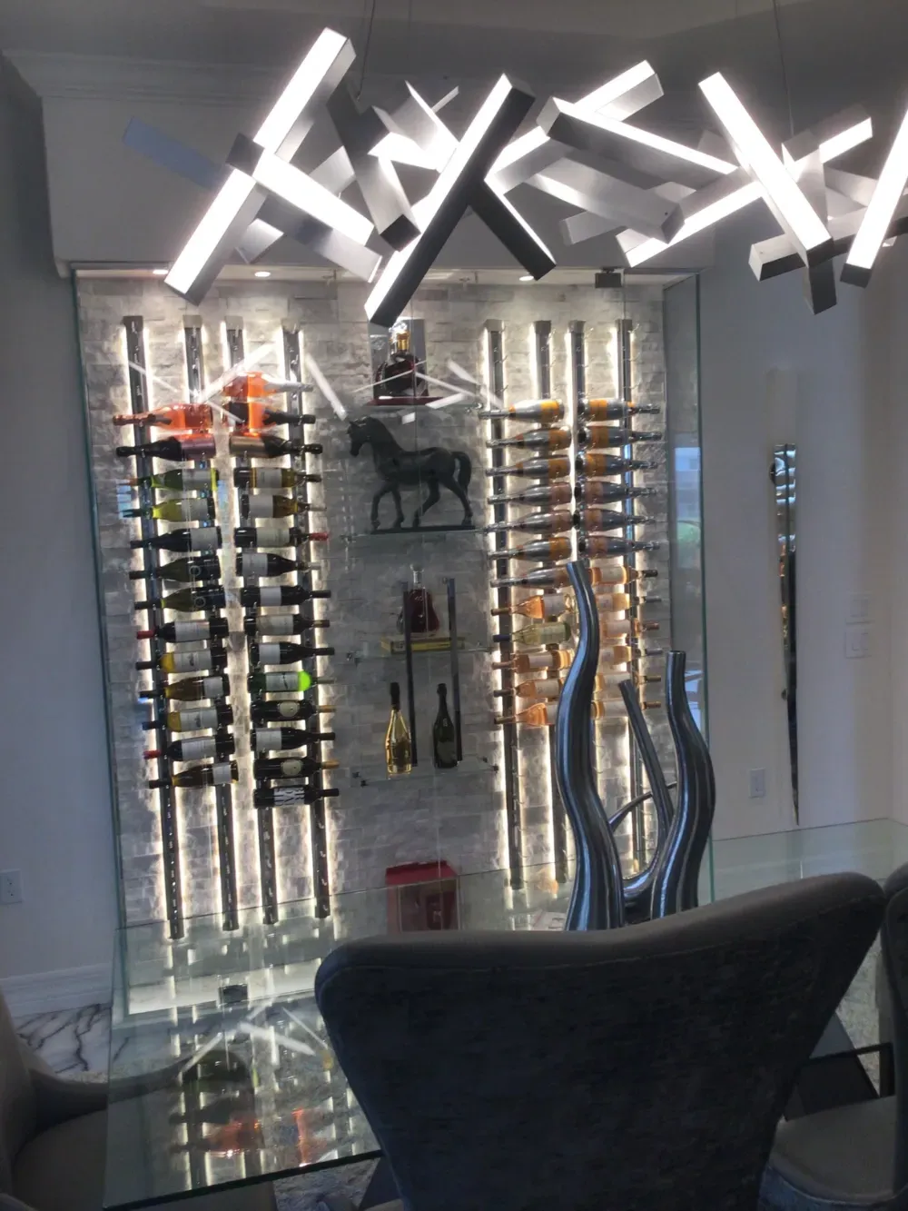 A modern wine display wall with backlit shelving and bottles, beneath an abstract, geometric light fixture.