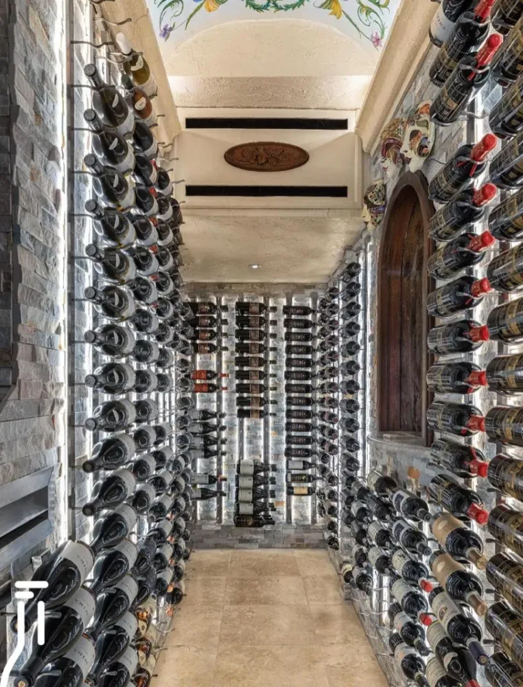 A long, narrow wine cellar with stone walls featuring floor-to-ceiling metal racks filled with wine bottles on both sides.