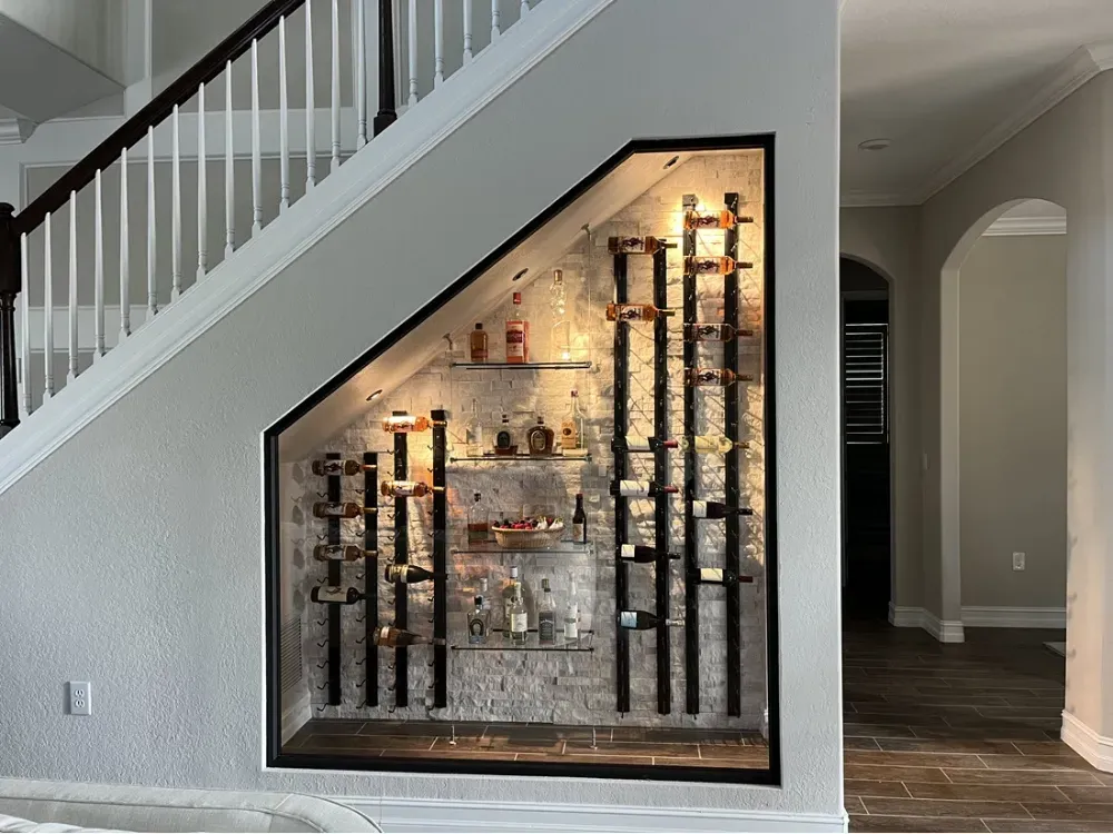A wine display built into the space under a staircase, featuring glass shelves, vertical wine racks, and accent lighting.