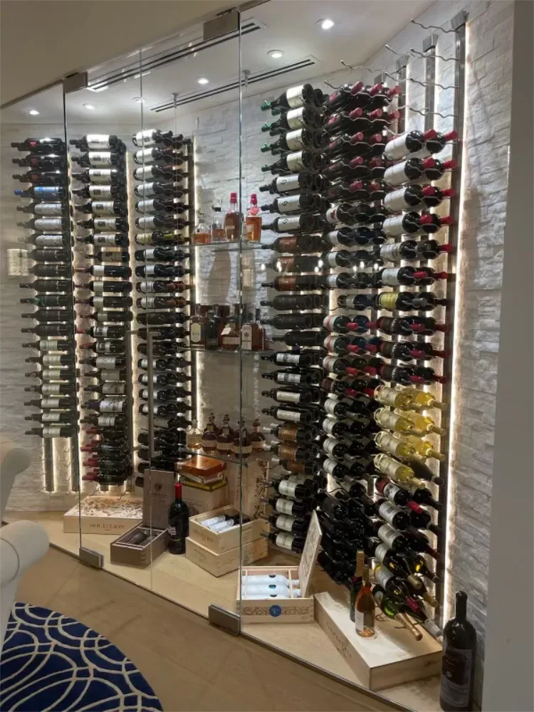 A modern, floor-to-ceiling glass wine cellar features multiple columns of horizontal bottle racks against a stone wall.