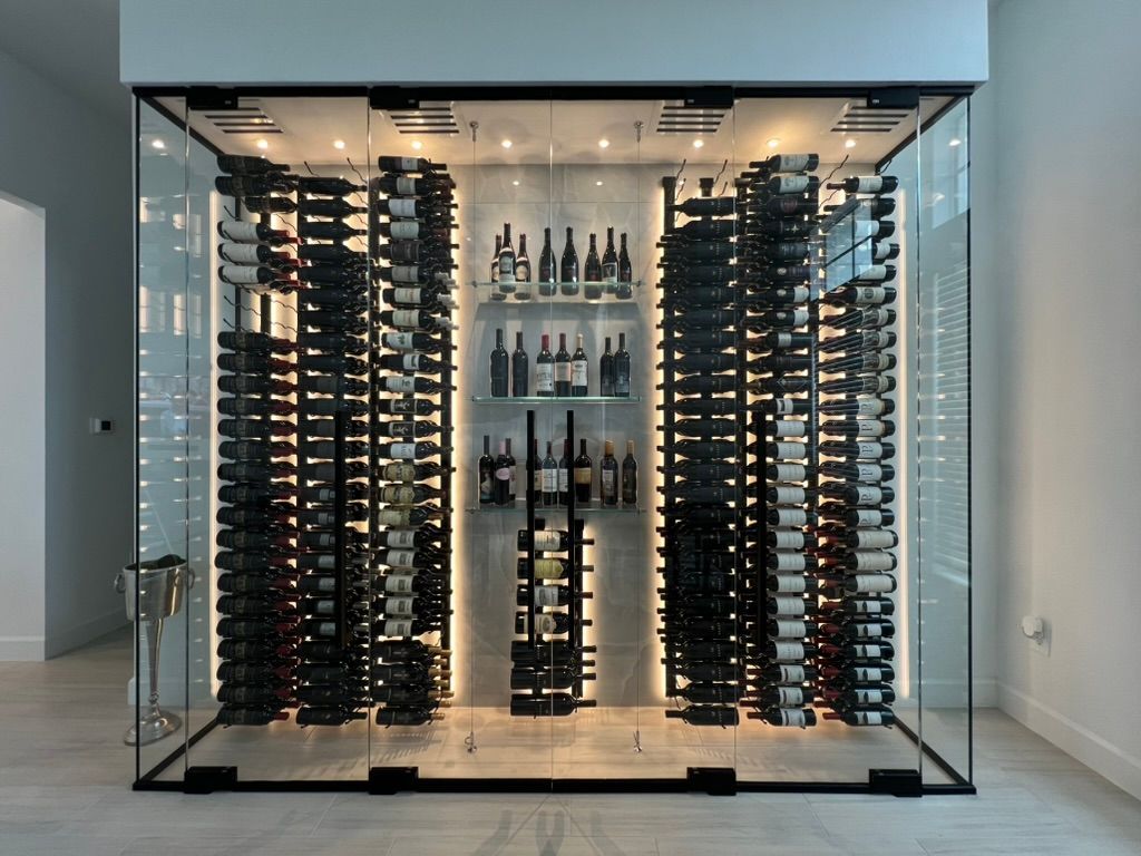 A modern, floor-to-ceiling glass wine cellar with black metal racks holding numerous bottles, illuminated by LED lights.