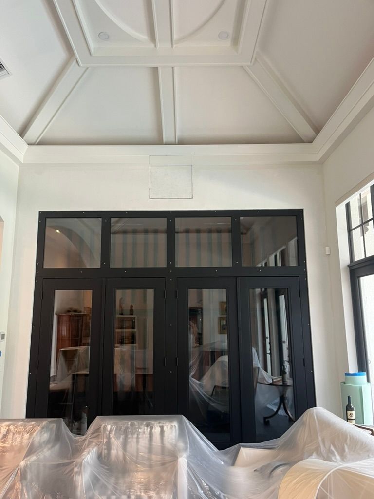 A high, ornate coffered ceiling above a black-framed glass wall and door partition in an interior room under construction.