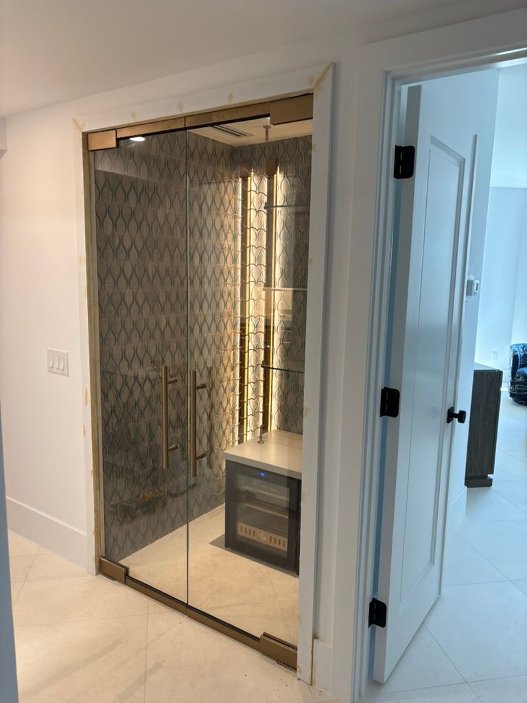 A walk-in glass wine cellar with metallic frames, decorative patterned tile walls, and a built-in wine cooler inside.