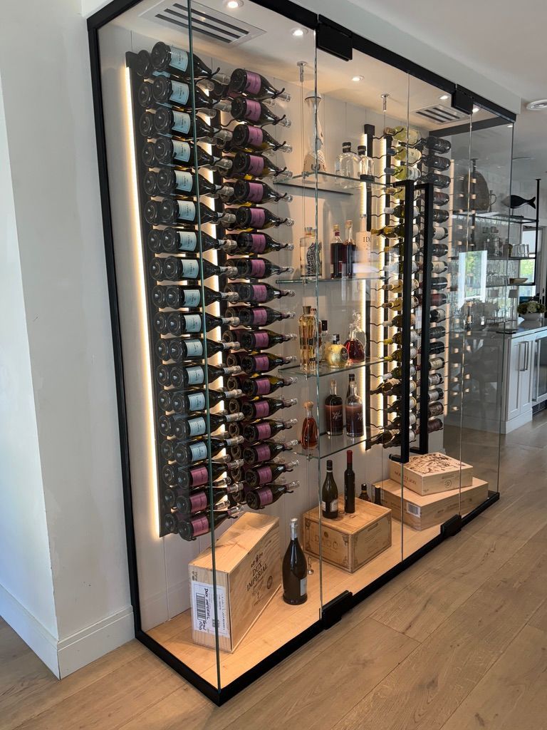 A modern, glass-enclosed wine display cabinet with vertical racks, LED backlighting, and wooden storage crates.