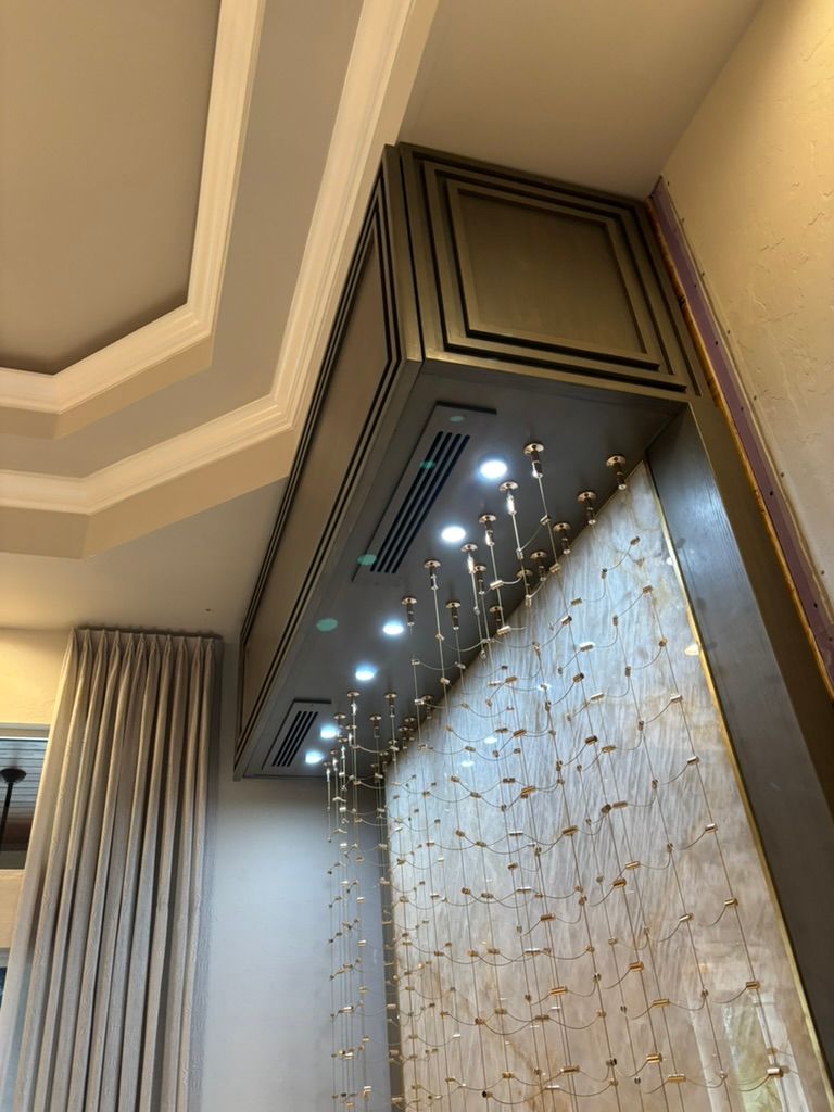A ceiling-mounted bronze architectural feature with recessed spotlights above a textured wall panel with hanging crystals.