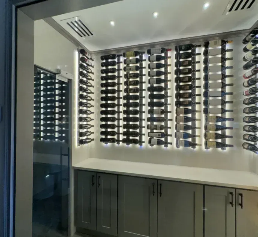Wine cellar with bottles displayed in wall racks, over cabinets, lit by recessed lights.
