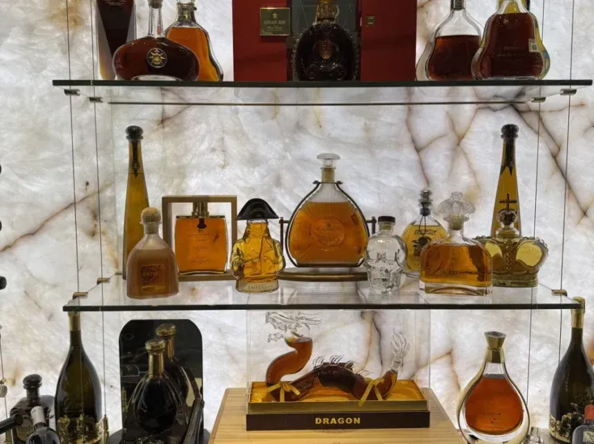 A display of various luxury glass bottles and decanters filled with amber-colored spirits on illuminated glass shelves.