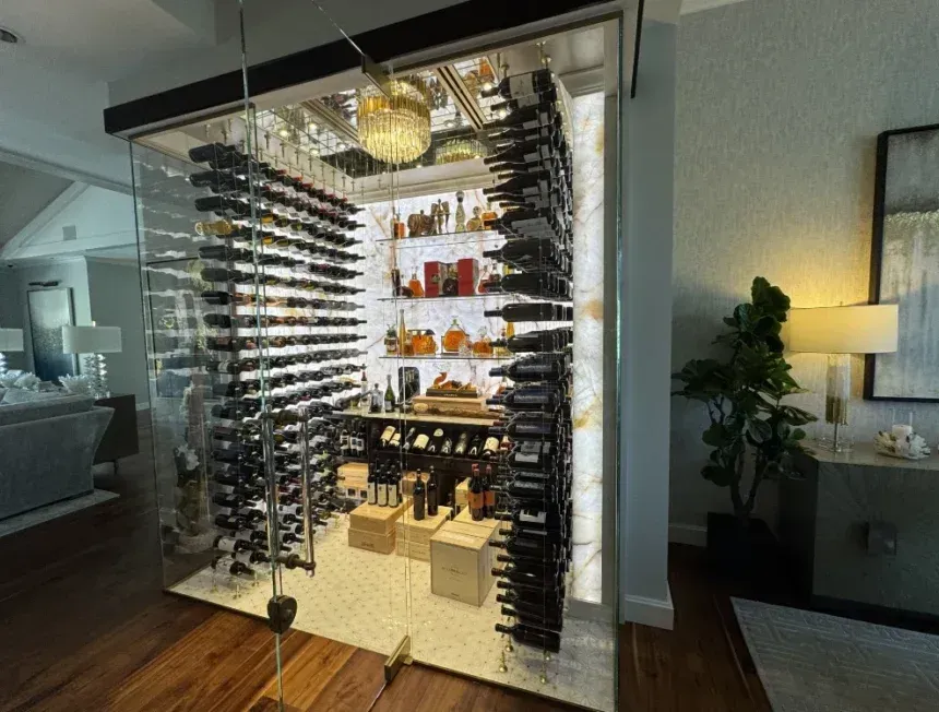 A glass-enclosed, climate-controlled wine cellar featuring floor-to-ceiling metal racks, LED lighting, and display shelves.