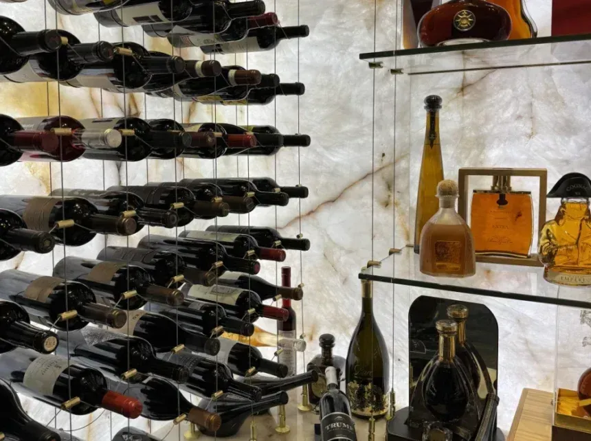 A wine cellar wall features horizontal wine racks on the left and illuminated glass shelves with liquor bottles on right.