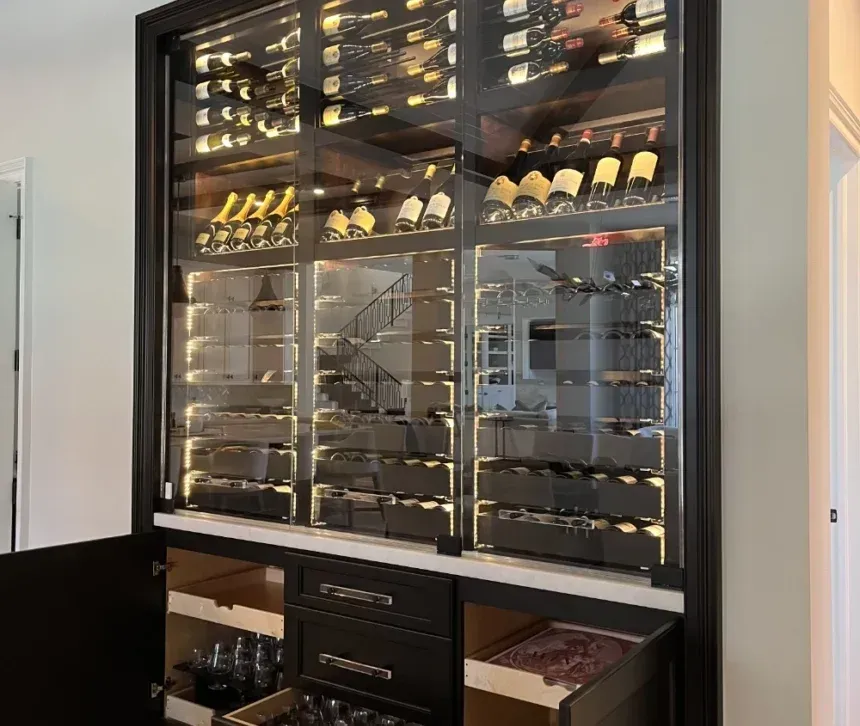 A dark wood cabinet featuring a glass-fronted, illuminated wine rack above storage drawers and open shelving.