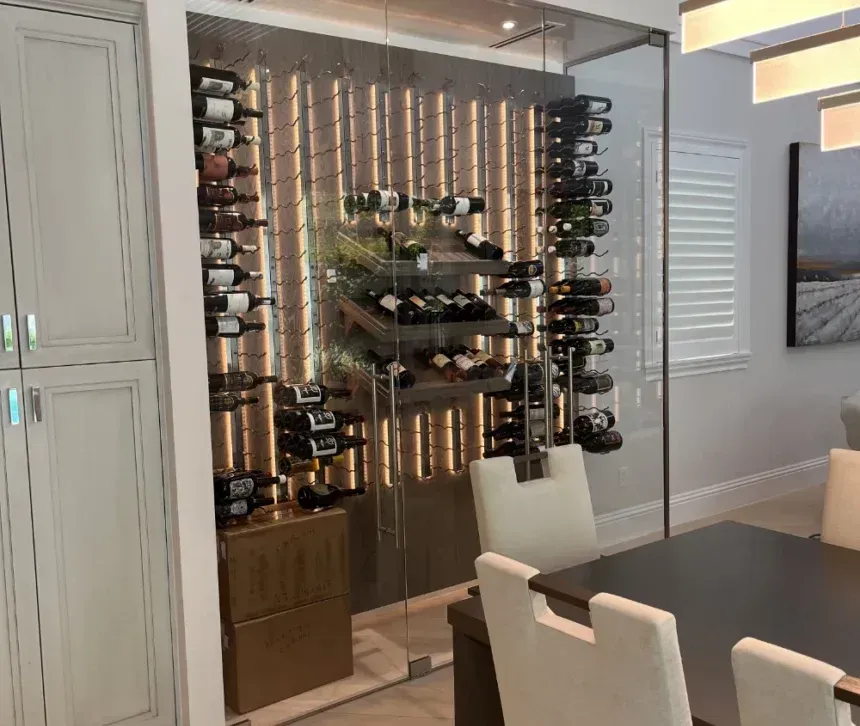 A climate-controlled wine display built into a wall beside a dining table, featuring rows of bottles on metal racks.