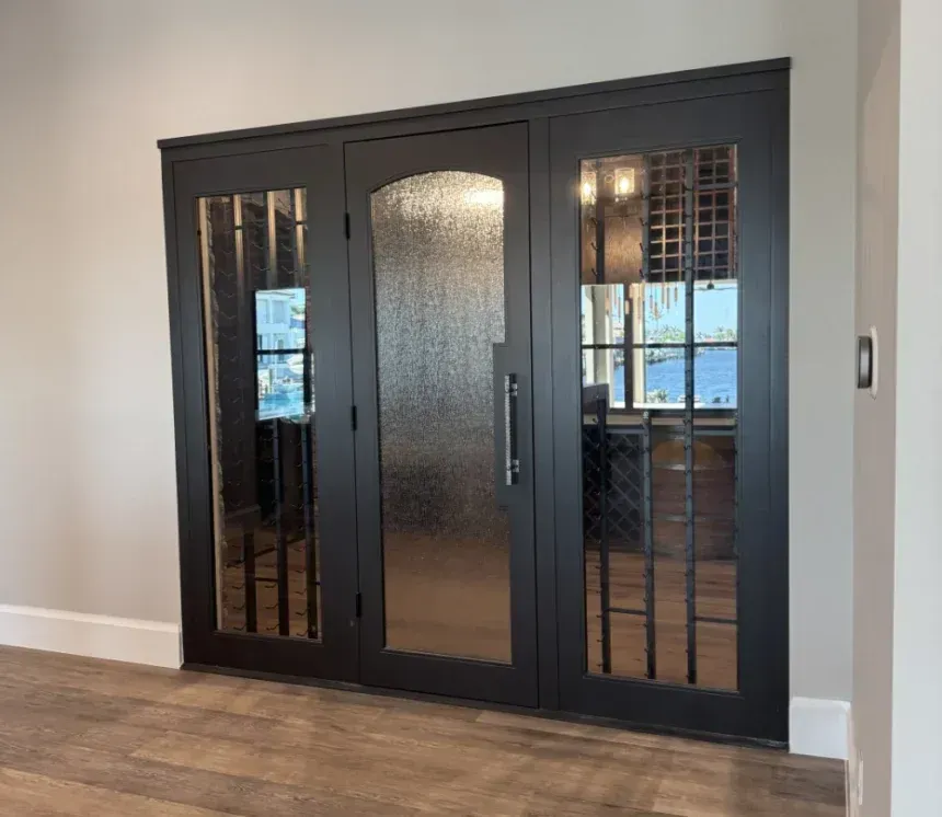 A modern, dark-framed three-panel door with a textured center glass pane and clear glass side panels featuring iron grilles.