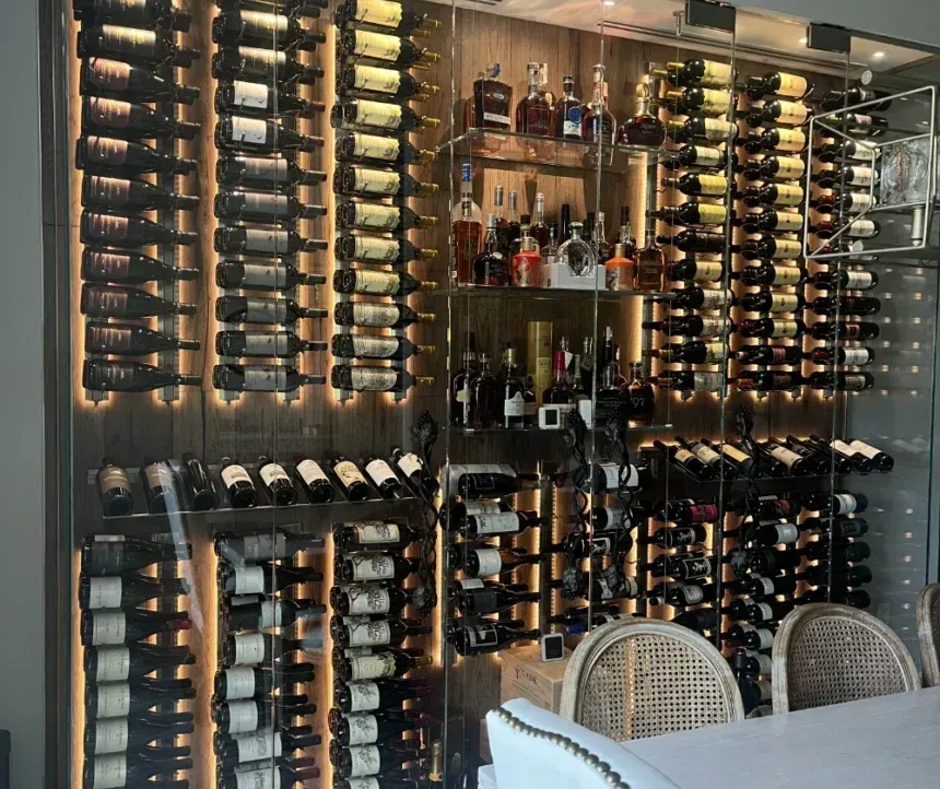 A wall-mounted wine rack display featuring rows of bottles, illuminated shelving for spirits, and chairs in front.