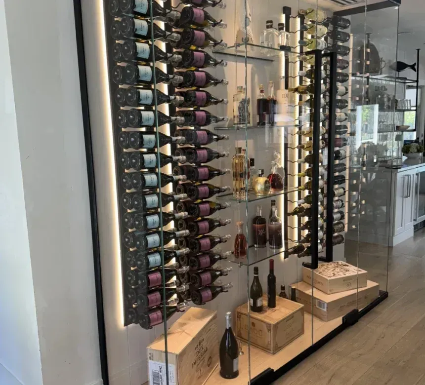 A glass-enclosed wine cellar with vertical racks holding bottles, middle shelves for display, and wooden crates on the floor.