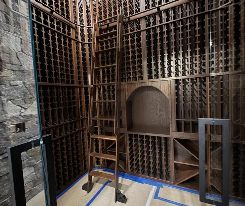 A wooden wine cellar with floor-to-ceiling grid shelving and a sliding ladder, set against a stone wall.
