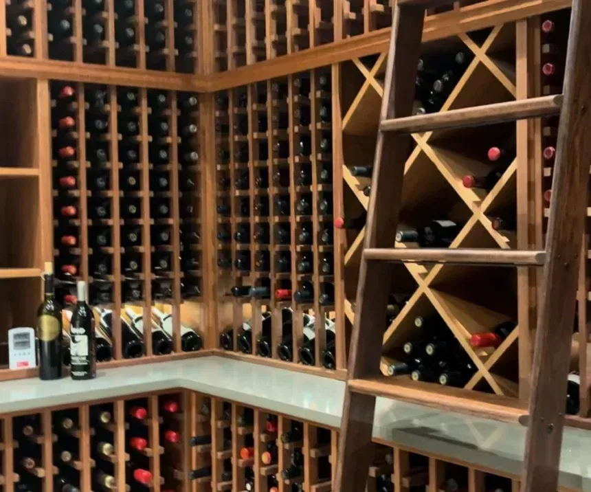 A wine cellar with wooden grid storage shelves, filled with wine bottles, featuring a wooden rolling ladder on the right.