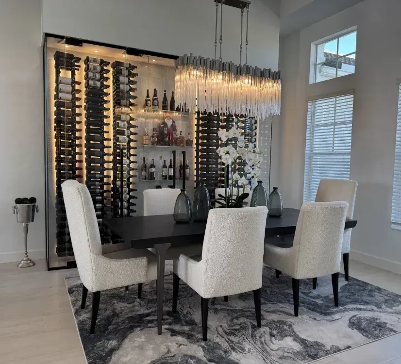 Dining room featuring a dark table, cream-colored chairs, a large crystal chandelier, and a lighted wine rack wall.