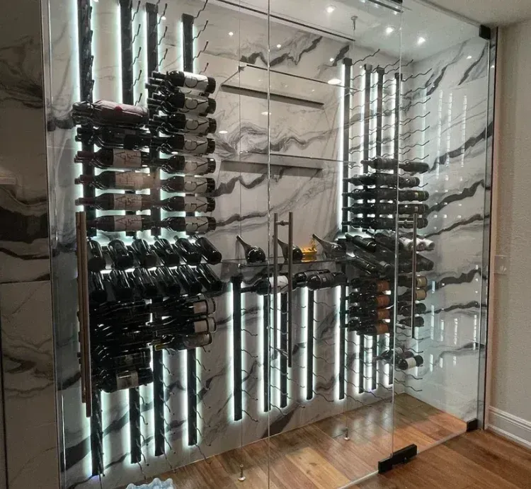 Modern wine cellar with horizontal bottle racks, integrated LED lighting, and white marble walls behind a glass door.
