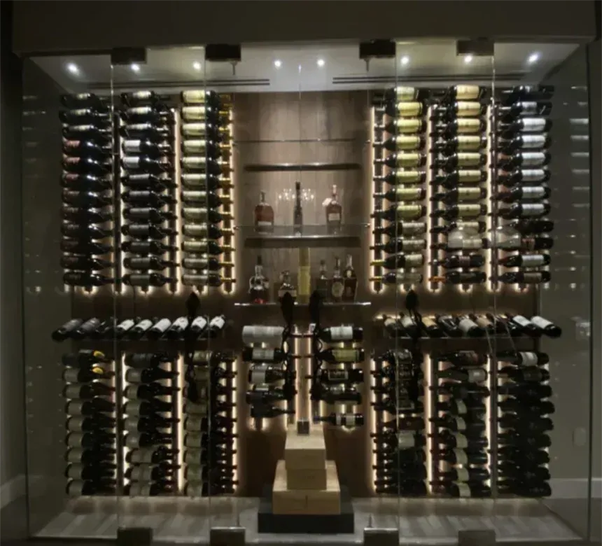 A wall-mounted glass wine cellar display featuring numerous rows of wine bottles illuminated by integrated lighting.