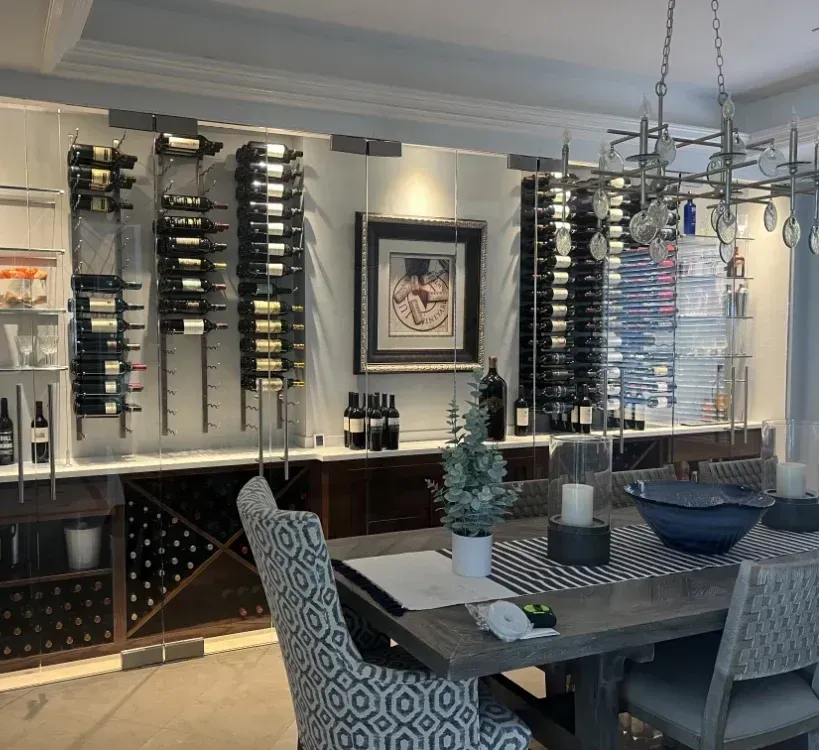 A dining room features a wall-mounted wine rack display with bottles, a central framed artwork, and a table with seating.