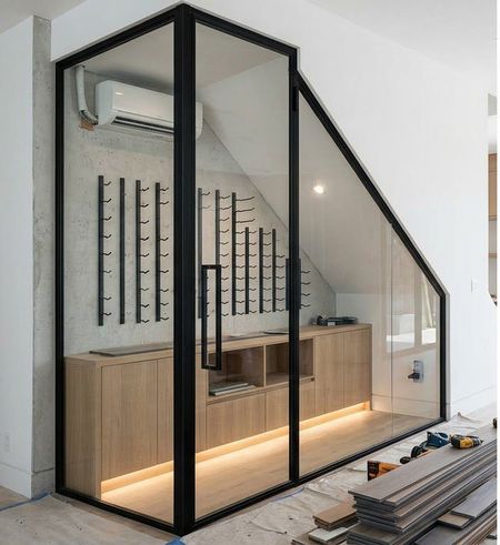 Modern, custom-built wine cellar with glass walls, black metal framing, light wood cabinets, and LED floor lighting.