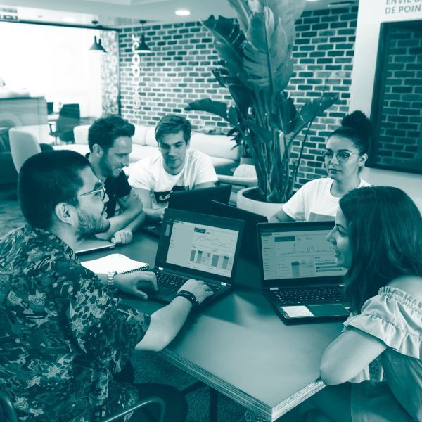 A group of people are sitting around a table with laptops