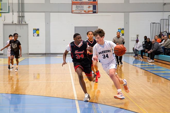 Basketball players sprint down the court during a game, one dribbling while another defends.