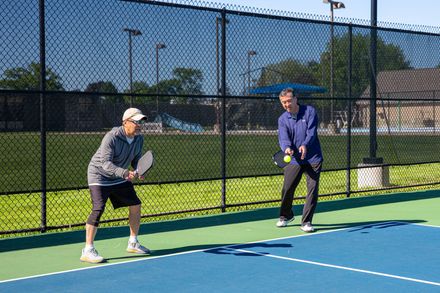 Two people ready to play pickleball on an outdoor court under a clear blue sky