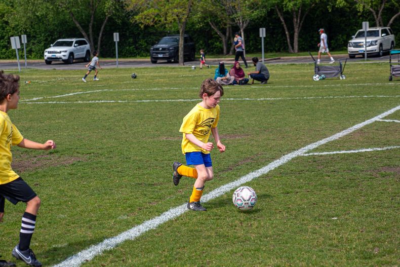 Child in yellow soccer jersey dribbling a ball on a grassy field during a youth game