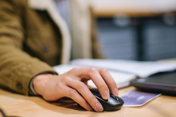 Hand on a wireless mouse at a desk beside a laptop and notebook