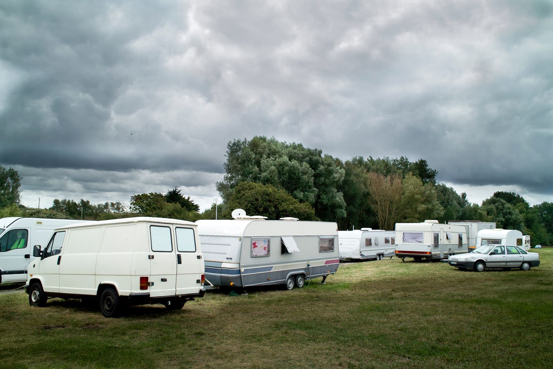 Une rangée de caravanes est garée dans un champ par temps nuageux