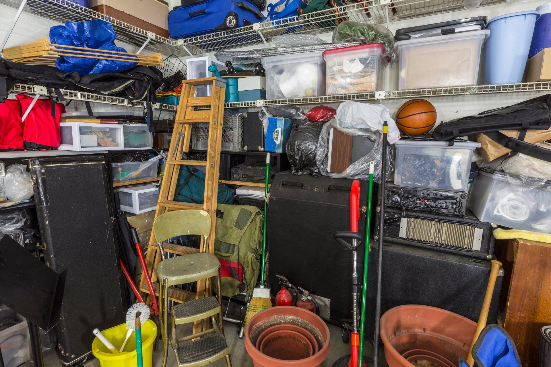 Messy residential garage packed full of boxes, tools and gardening items.