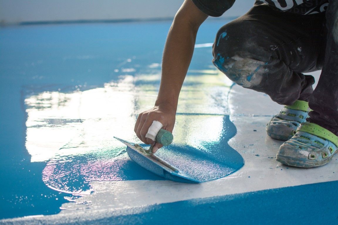 Person spreading blue paint on a glossy floor with a roller brush
