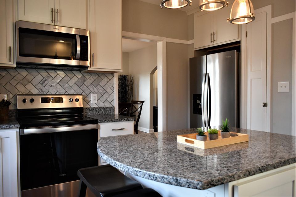 A kitchen with granite counter tops , stainless steel appliances , and white cabinets.