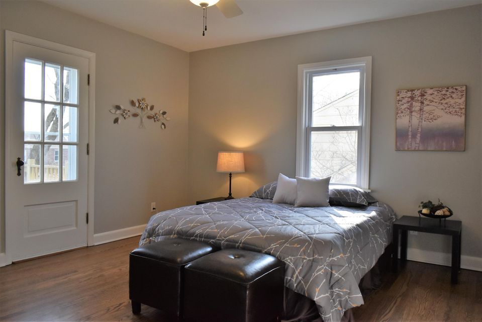 A bedroom with a bed , two ottomans , a lamp and a window.