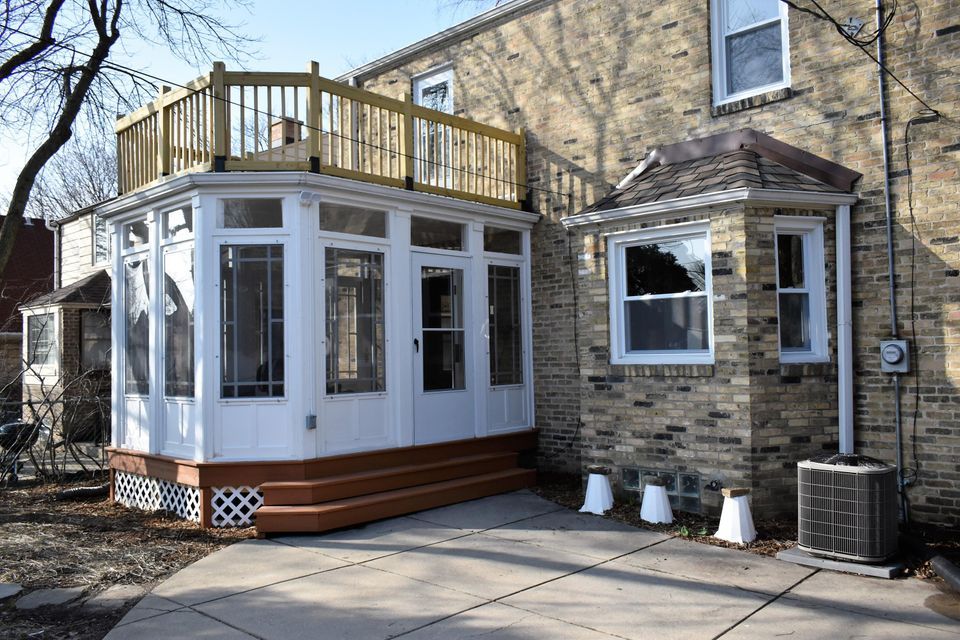 A brick house with a sunroom and a wooden deck