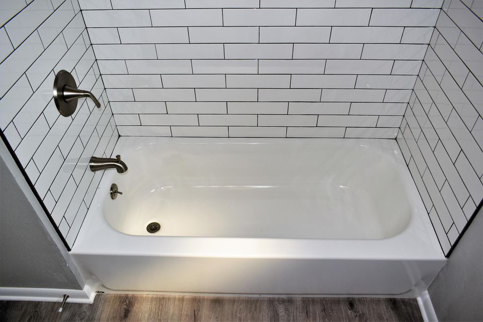 A bathtub in a bathroom with white tiles on the wall.