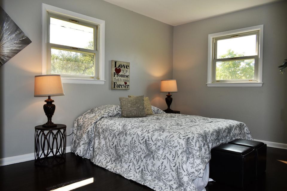 A bedroom with a bed , two lamps , and two windows.