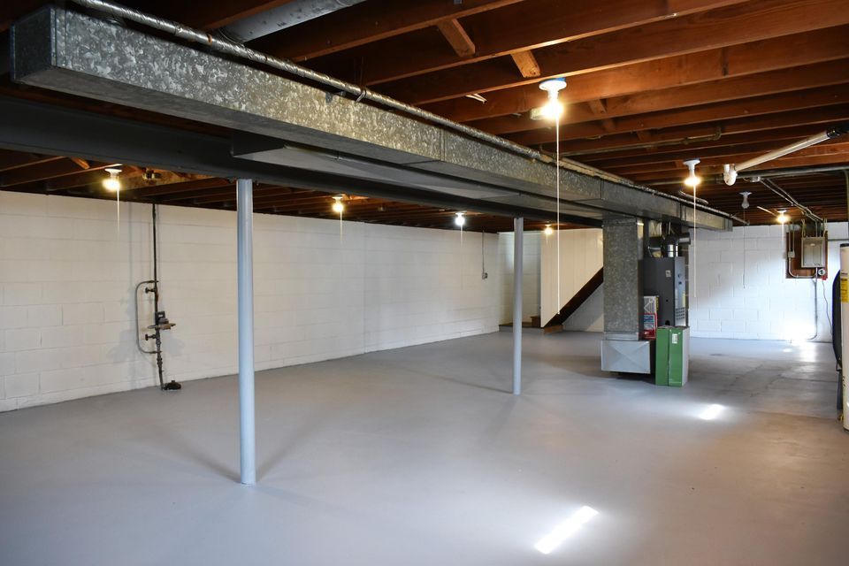 An empty basement with white walls and a wooden ceiling.