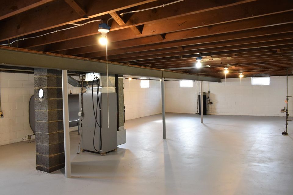 An empty basement with a wooden ceiling and a refrigerator.