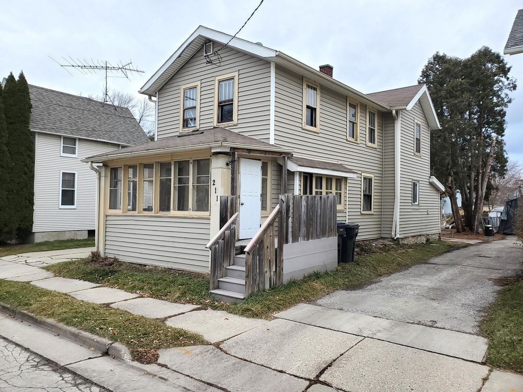 A house with stairs leading up to the front door is sitting on the corner of a street.