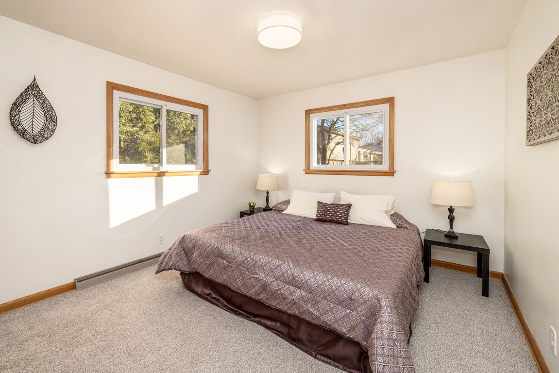 A bedroom with a bed, lamps, and two windows.