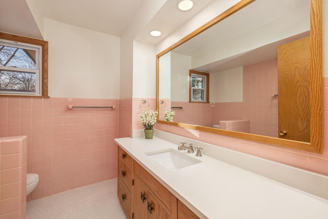 A bathroom with pink tiles and a large mirror.