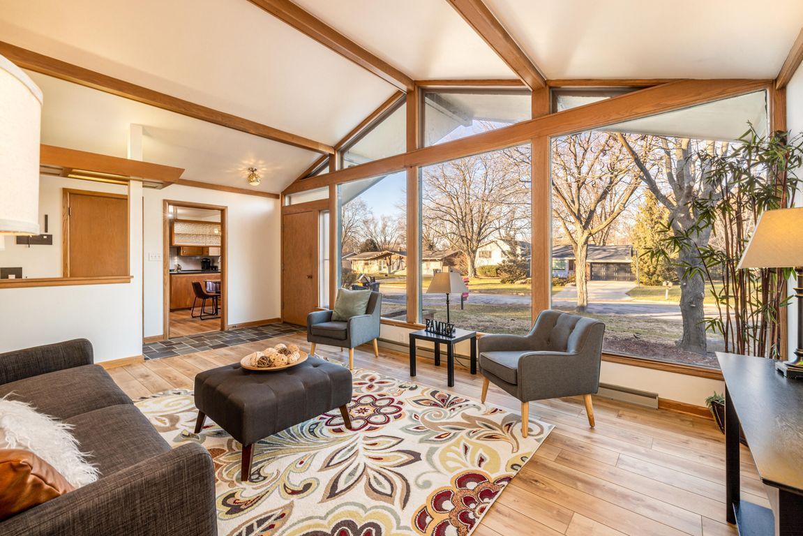 A living room with a couch , chairs , ottoman and large windows.