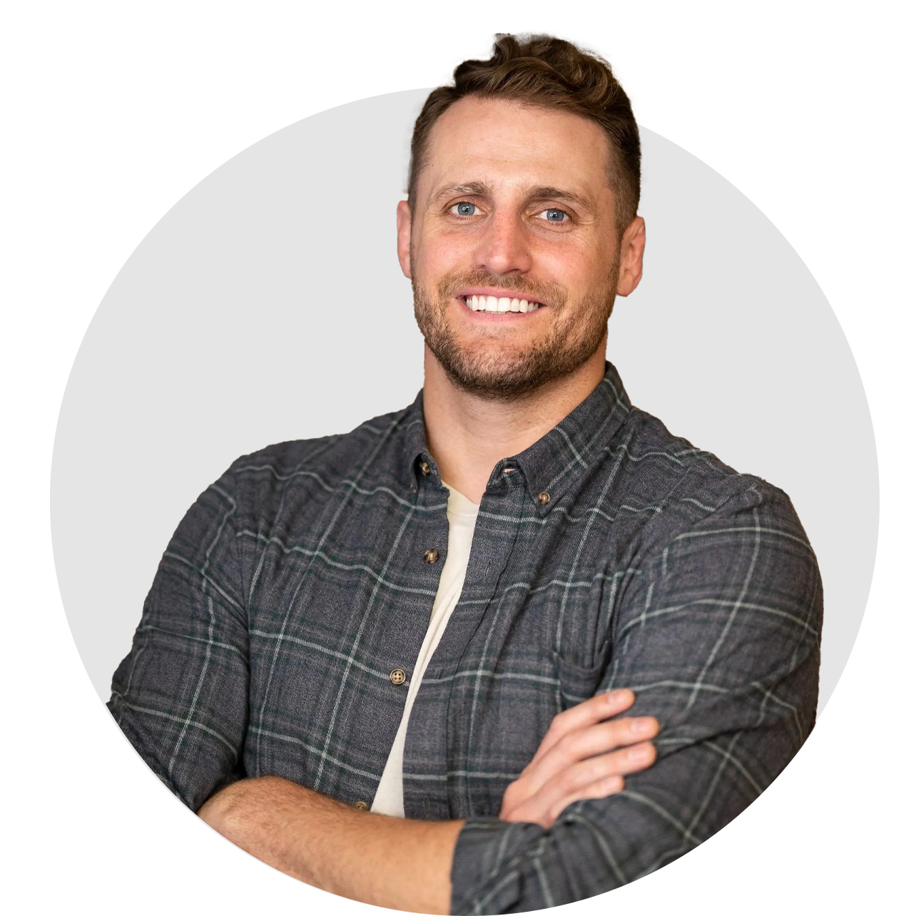 A man in a plaid shirt is smiling with his arms crossed.