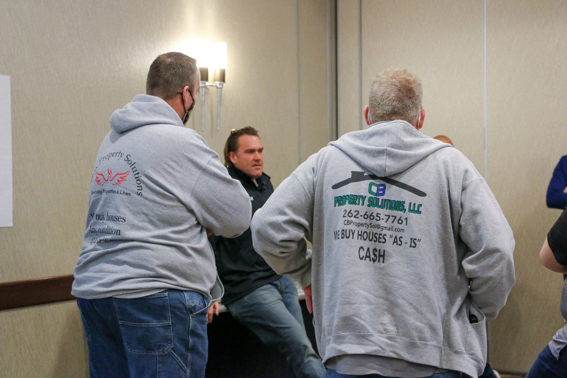 A group of men are standing in a room and one of them is wearing a hoodie that says impact builders