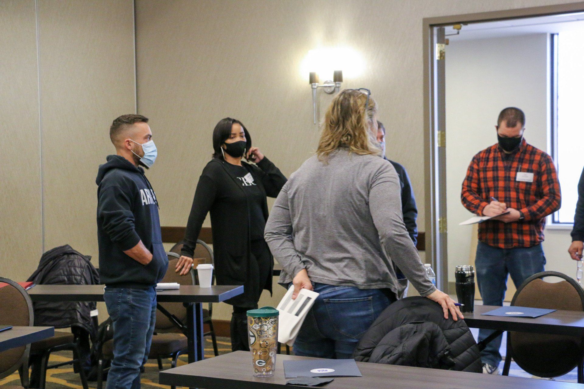 A group of people wearing face masks are standing around tables in a room.